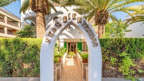A white arched entrance with the words "BIENEN AVENIROS" carved into it, leading to a building with balconies and a green door. - Hotel Martorell (Ses Salines)