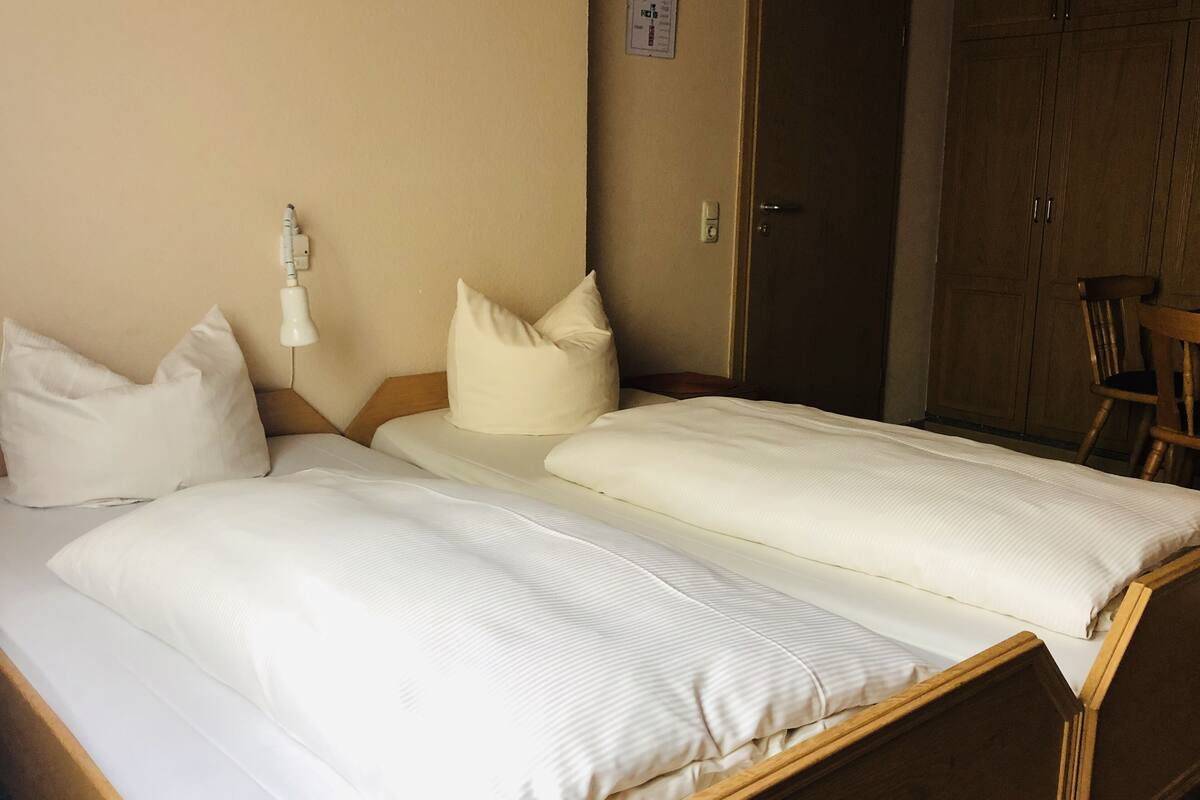 A hotel room with two single beds, a wooden wardrobe, and a small table.