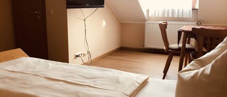 Un dormitorio con una cama, un televisor montado en la pared, una mesa de madera y una silla.