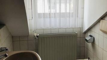A small bathroom with a toilet, a sink, a window with a curtain, and a radiator.