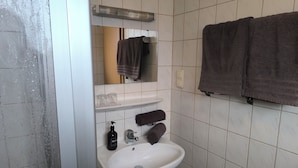 Baño con lavamanos blanco, un espejo, toallero con dos toallas y estante con dos vasos de vidrio.