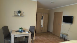 Habitación de hotel con cama, mesa de madera con sillas, televisor montado en la pared y armario.
