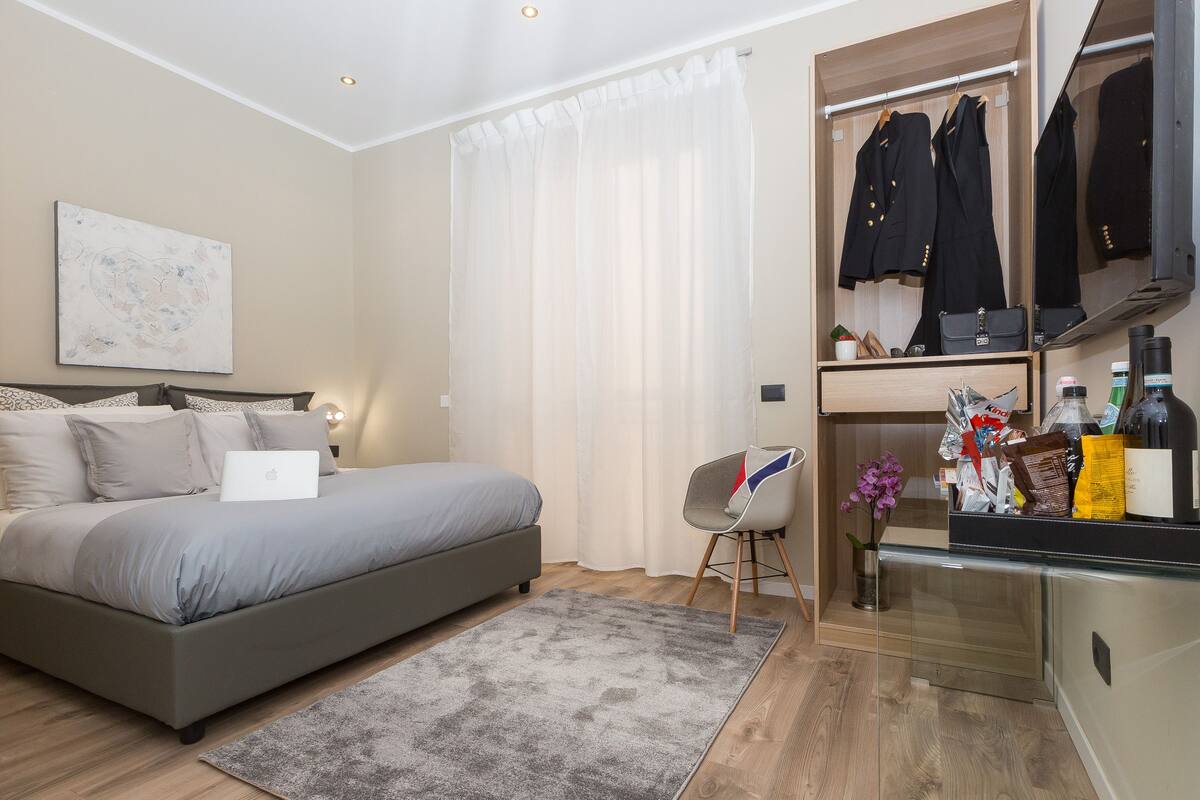 A bedroom with a bed, a desk, a chair, and a closet with hanging clothes.