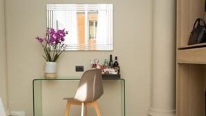 Una habitación moderna con un escritorio de cristal, una silla, una orquídea en maceta, un espejo y una estantería con botellas y una caja.