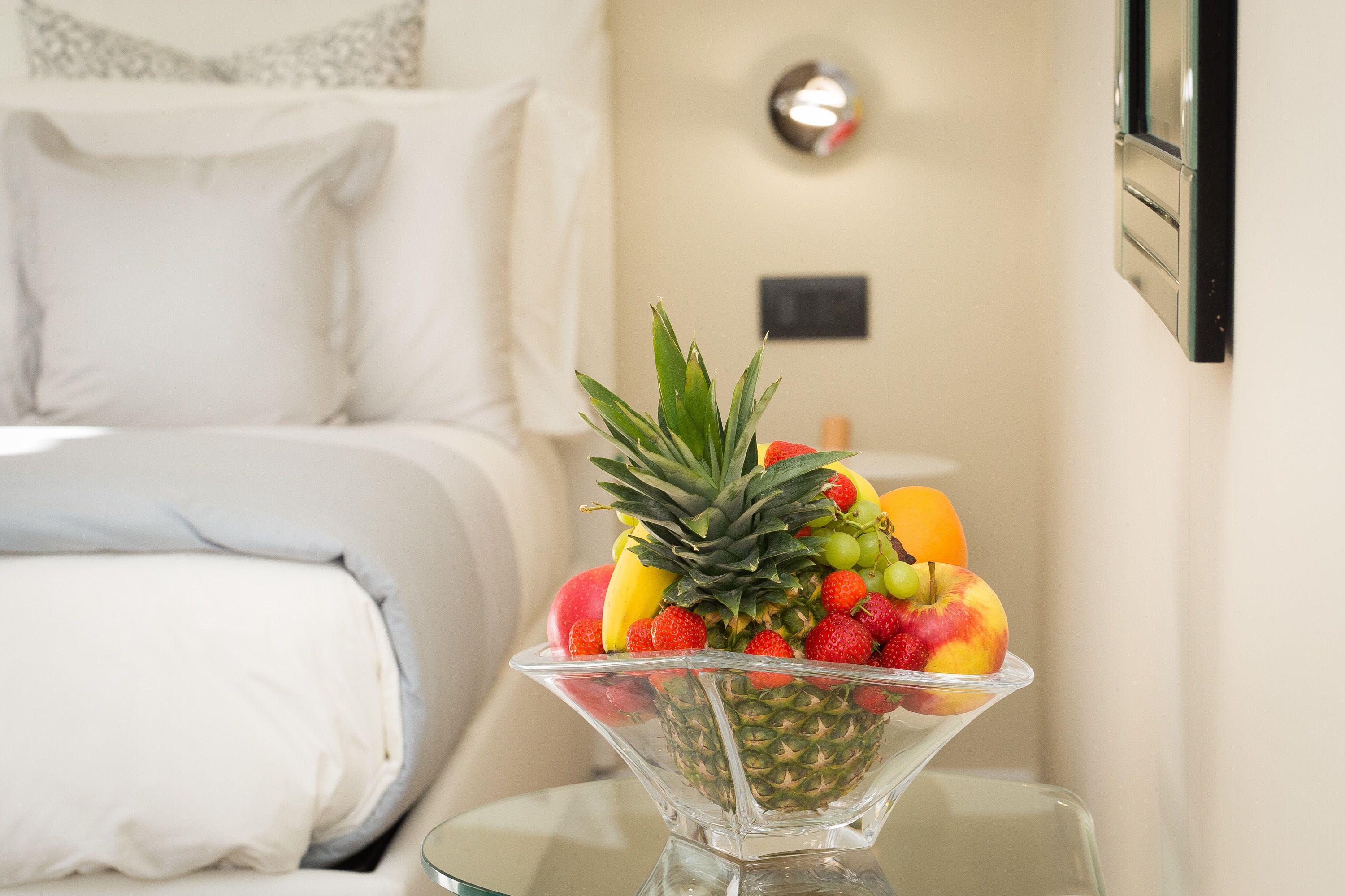 Una camera d'albergo con un letto, un comodino e una ciotola di frutta sul comodino.