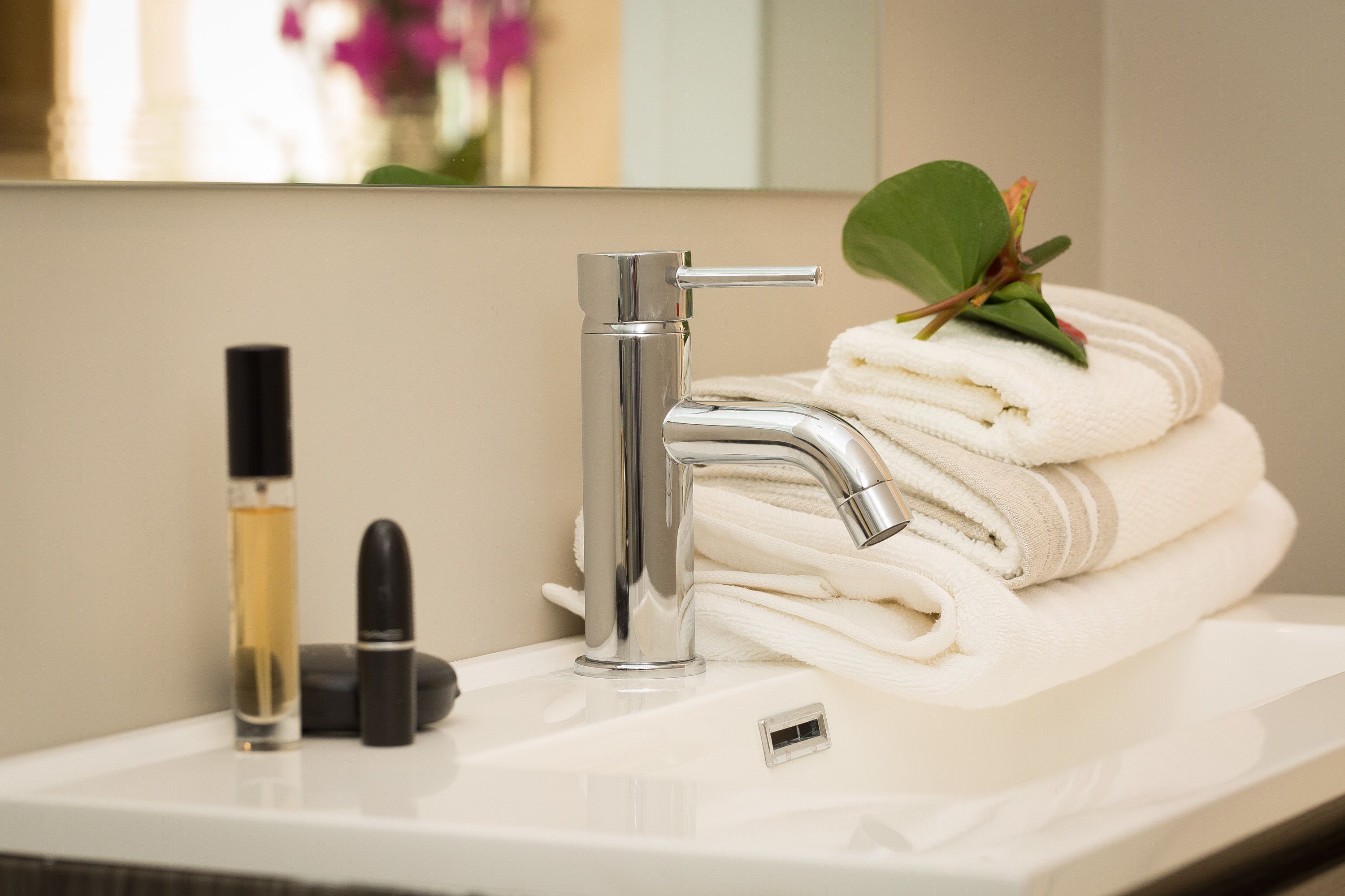 A bathroom sink with a modern faucet, a bottle of perfume, and a folded towel.