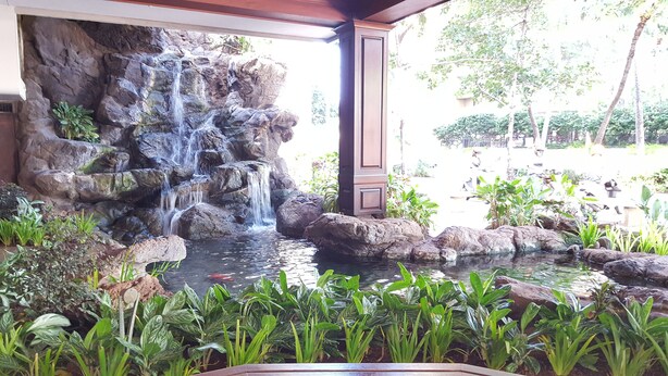 A waterfall feature with a rocky backdrop and a small pond in a landscaped area with various plants. - HAWAII  2 MIN FROM THE BEACH (Honolulu)