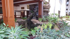 A hotel entrance with a stone waterfall, a sign indicating 'Tower 1 Makai', and a variety of tropical plants. - HAWAII  2 MIN FROM THE BEACH (Honolulu)