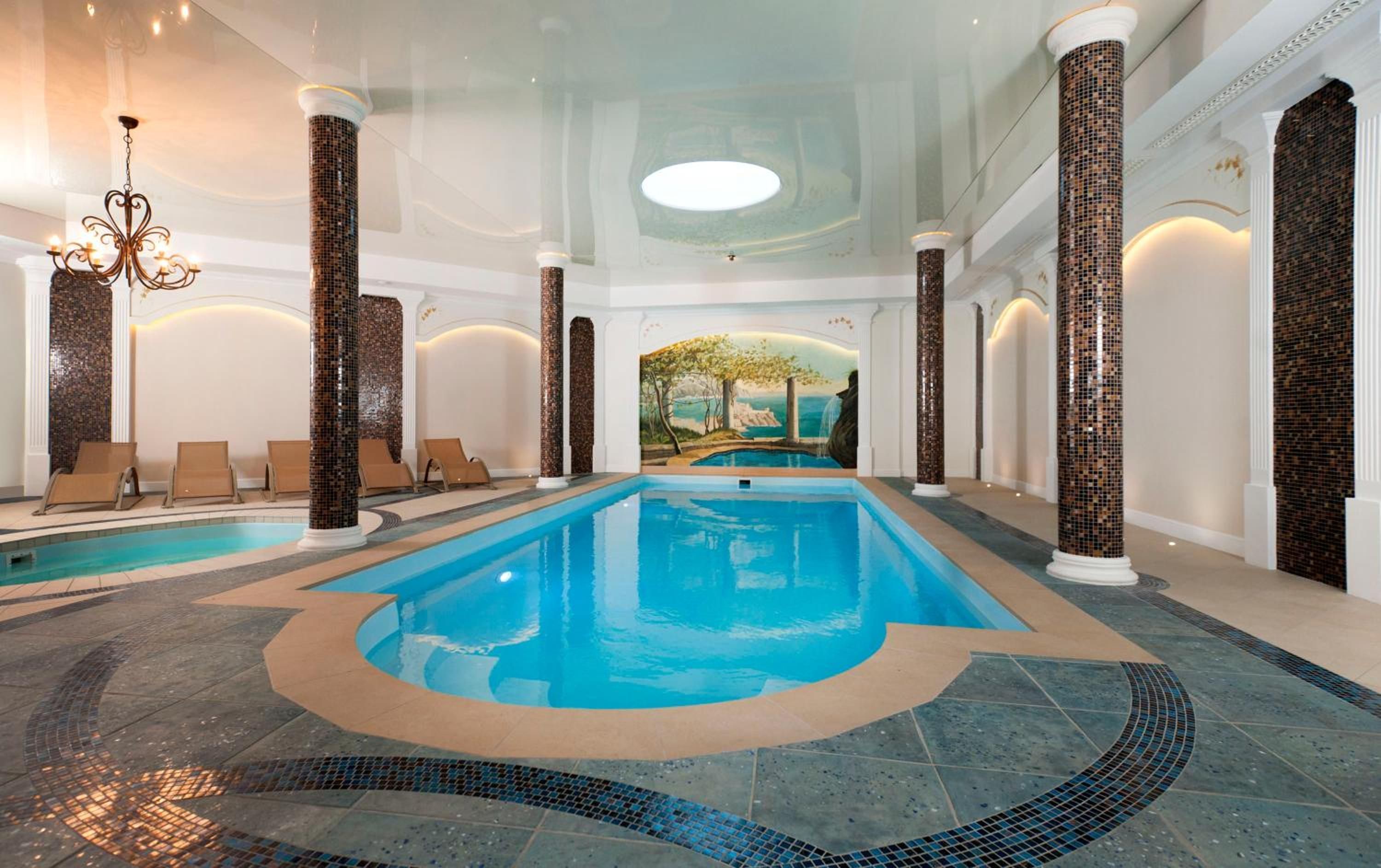 An indoor swimming pool with a mural, lounge chairs, and columns.