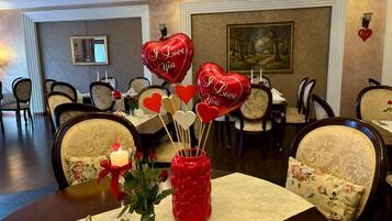 A dining table set with a candle, a vase with roses, heart-shaped balloons, and a decorative sign with the word 'love'.
