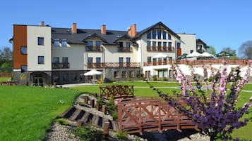 A multi-story hotel with a stone facade, outdoor seating, and a garden area with a wooden bridge.