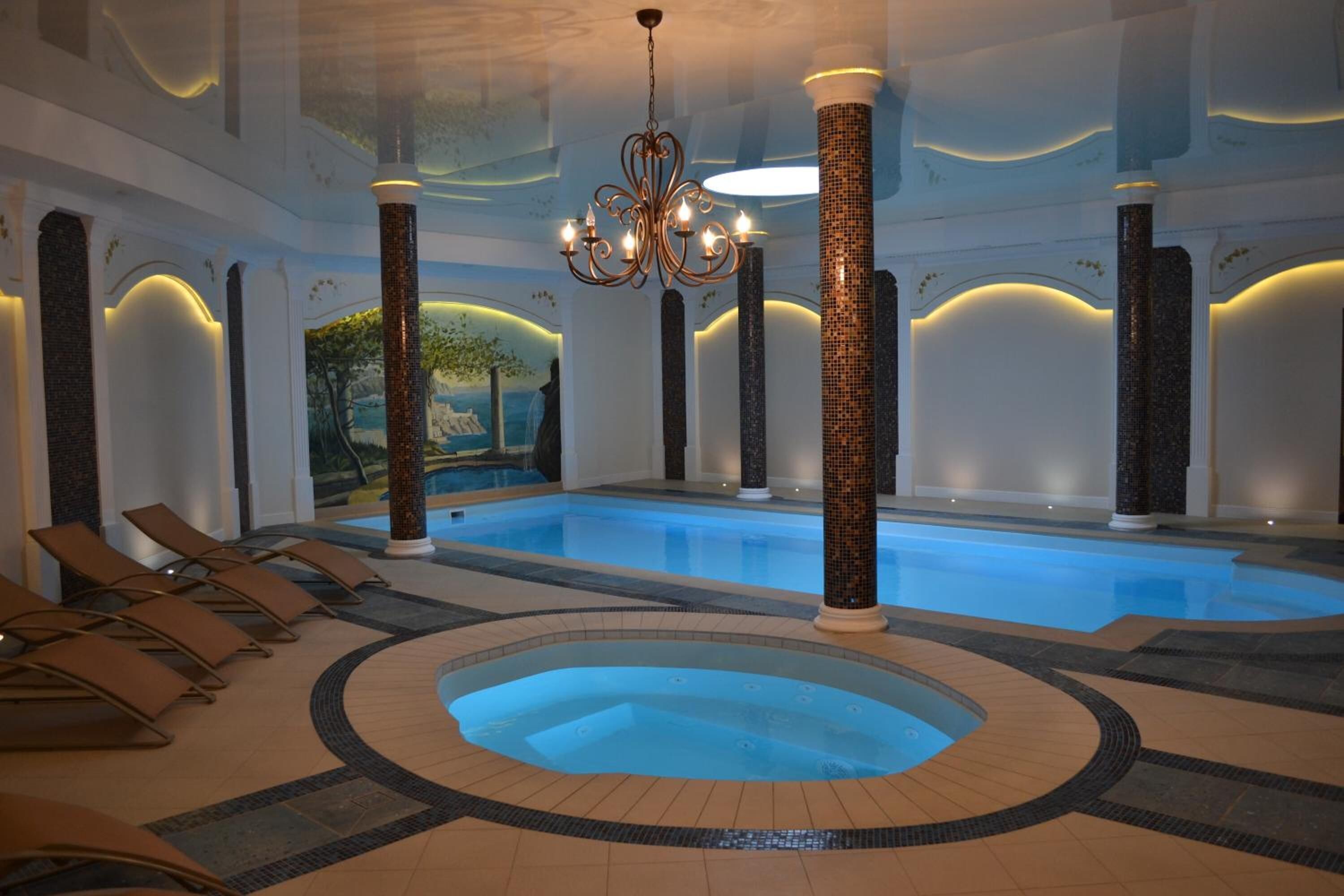 Una piscina interior amb un banyera d'hidromassatge, gandules i columnes decoratives.