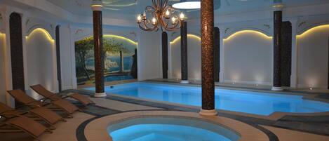 Una piscina interior amb un banyera d'hidromassatge, gandules i columnes decoratives.