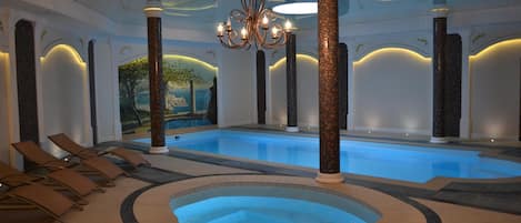 Una piscina interior con jacuzzi, sillas de descanso y columnas decorativas.