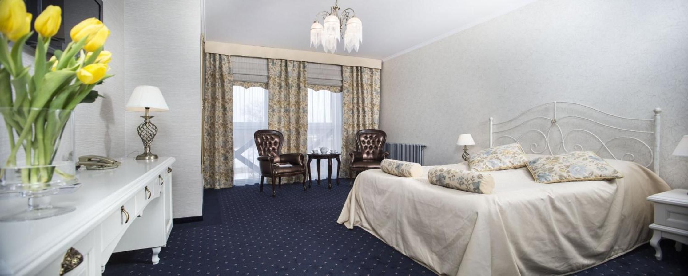 A hotel room with a bed, two chairs, a small table, a dresser, and a vase of flowers.