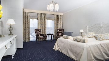 A hotel room with a bed, two chairs, a small table, a dresser, and a vase of flowers.