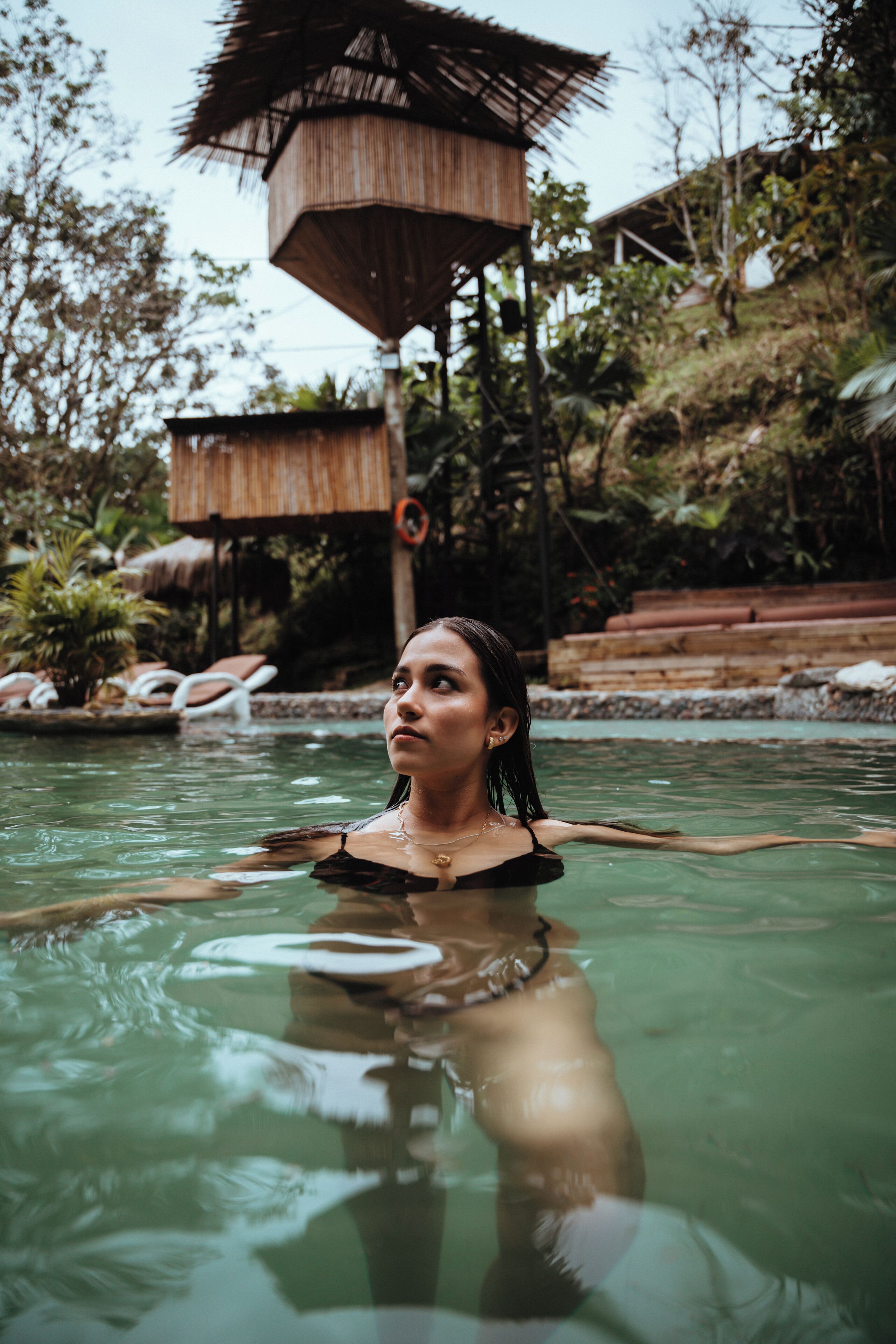 Una mujer en una piscina con una estructura de madera al fondo.