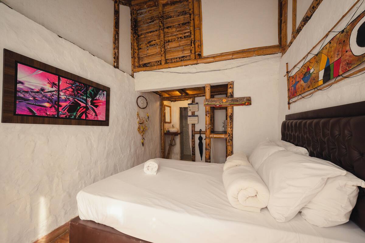 A bedroom with a bed, a painting on the wall, and a wooden ceiling.