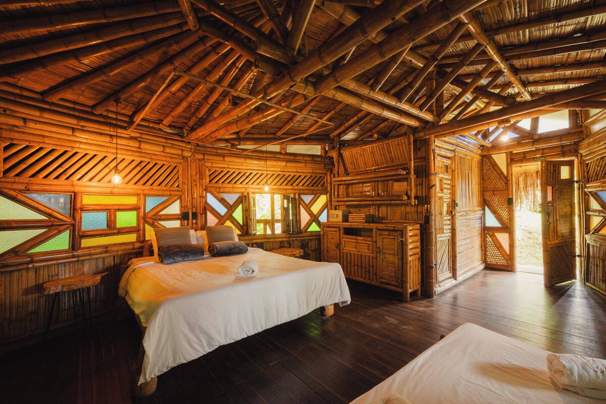 A wooden cabin with a large bed, a small table, and a window with a view.