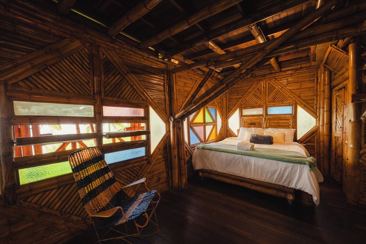 A room with a bed, a chair, and large windows with a view.