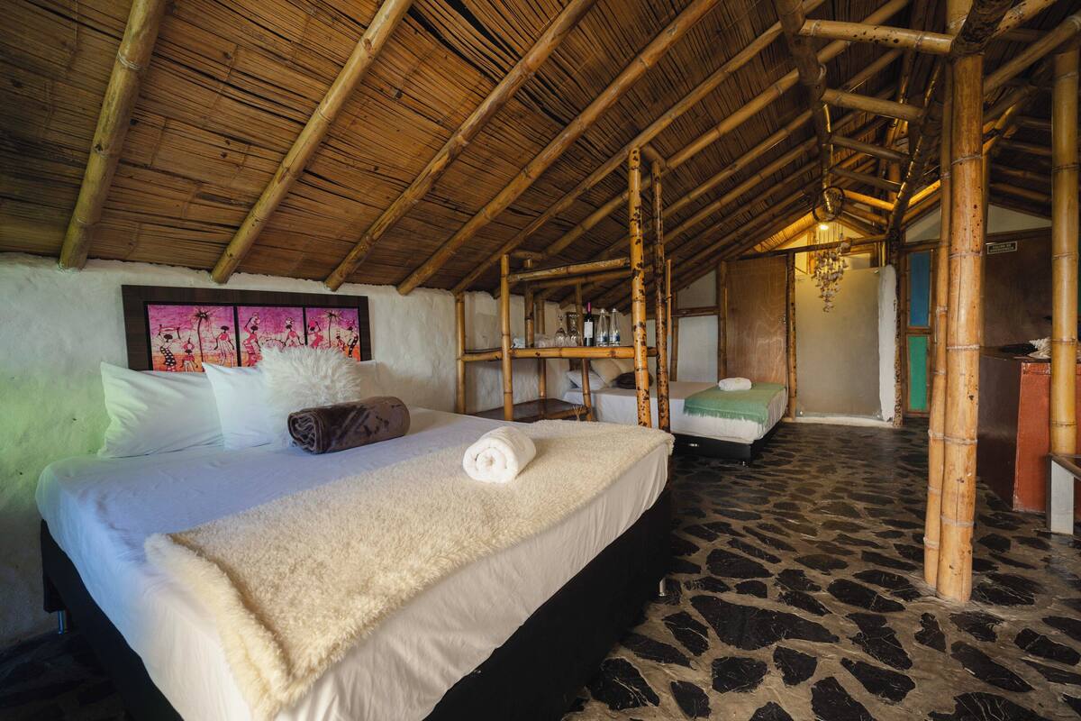 A room with a bed, a wooden ceiling, a shelf with bottles, and a patterned floor.