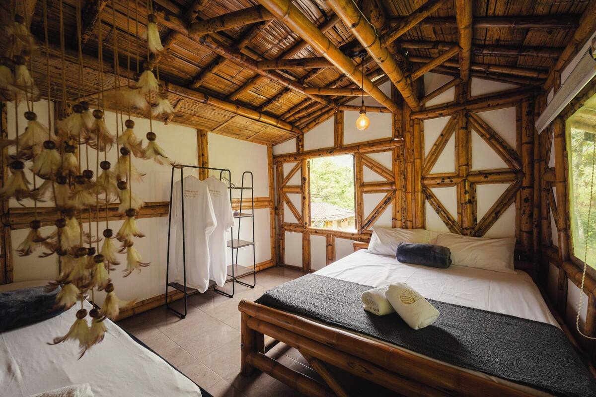 A room with a bed, a hanging light fixture, a wooden ceiling, and a window.