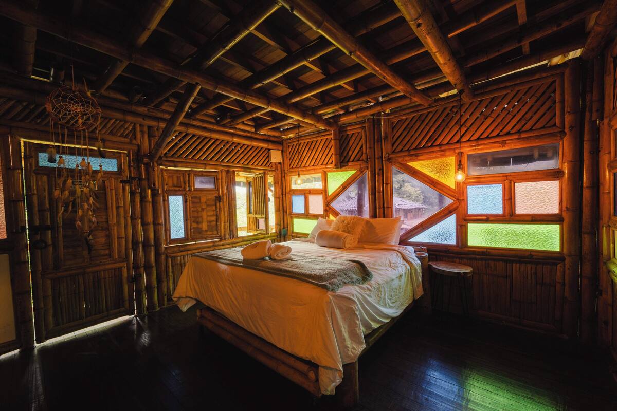 A wooden cabin-style room with a bed, windows, and a hanging dreamcatcher.