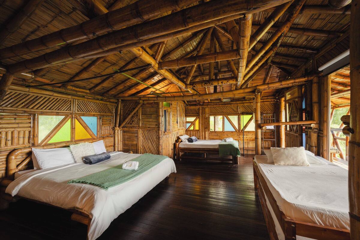 A room with two beds, wooden flooring, and a high ceiling with exposed beams.
