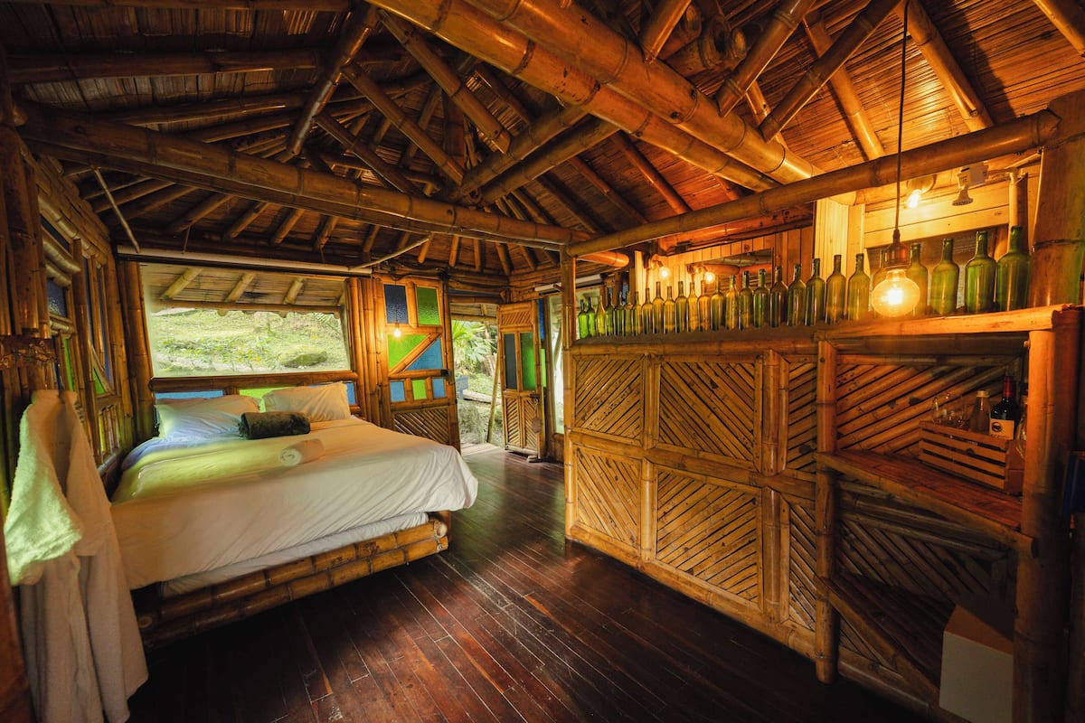 A room with a bed, wooden walls, and a shelf with bottles.