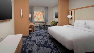 A hotel room with a large bed, a desk, a chair, a TV, and a window with curtains.
