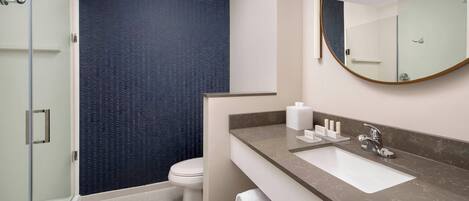 Un baño moderno con cabina de ducha de vidrio, inodoro blanco y encimera de mármol con lavabo y espejo.