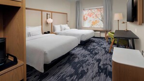 A hotel room with two beds, a desk, a chair, a TV, and a window with a view of trees.