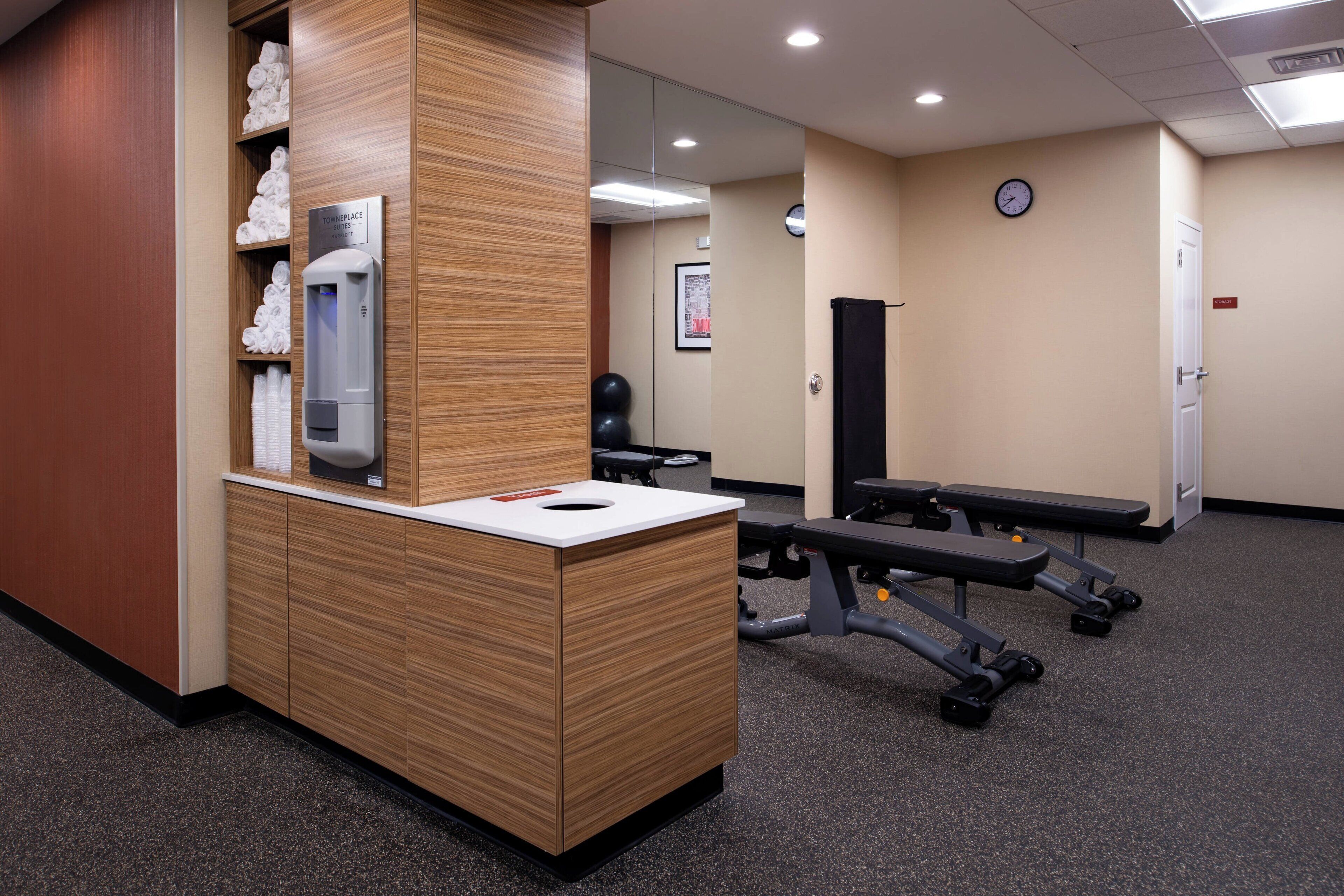 Zona de recepción con un mostrador de madera, dispensador de toallas, un reloj y equipo de ejercicios.