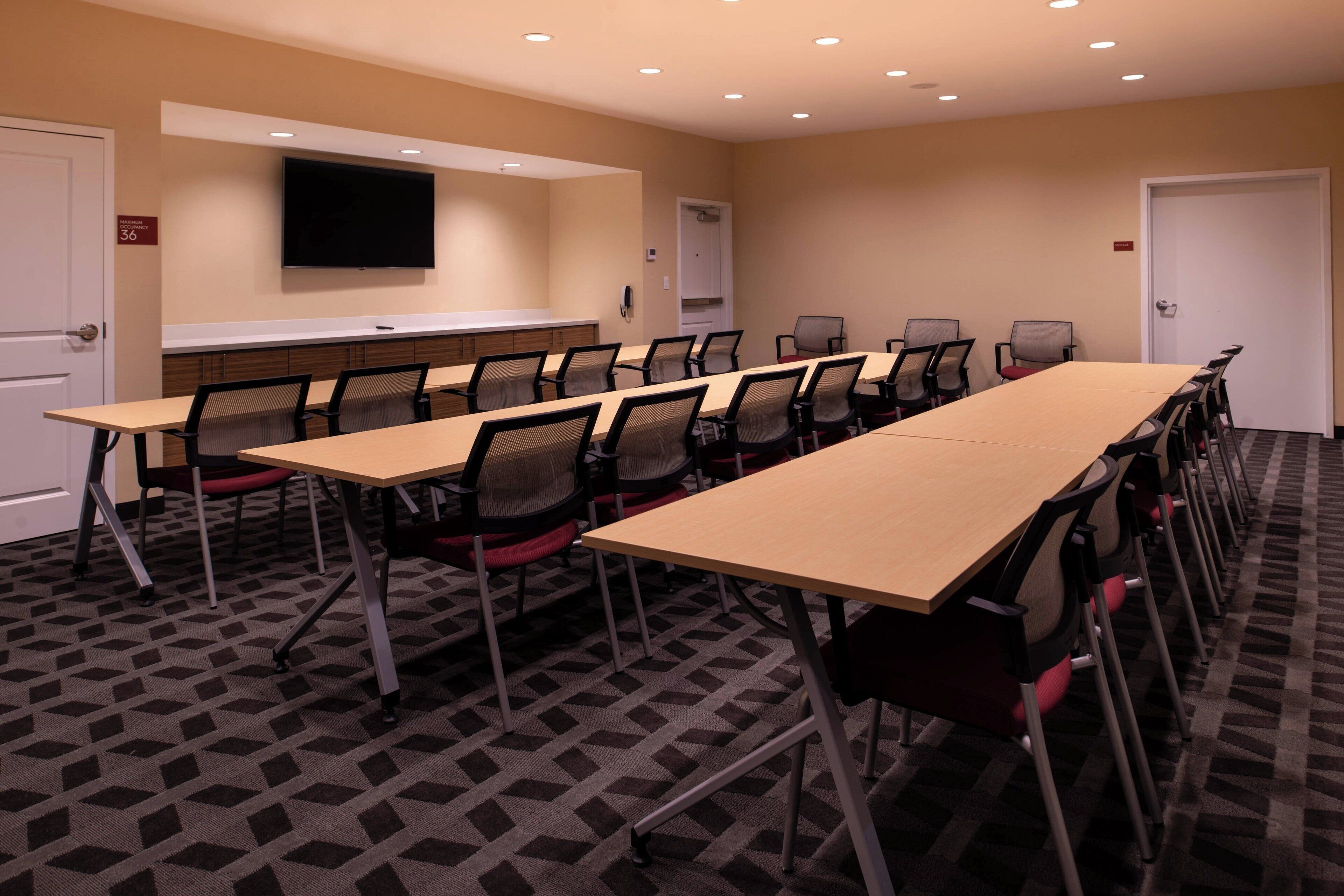 A conference room with a long table, chairs, a flat-screen TV, and a carpeted floor.