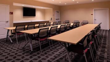 A conference room with a long table, chairs, a flat-screen TV, and a carpeted floor.