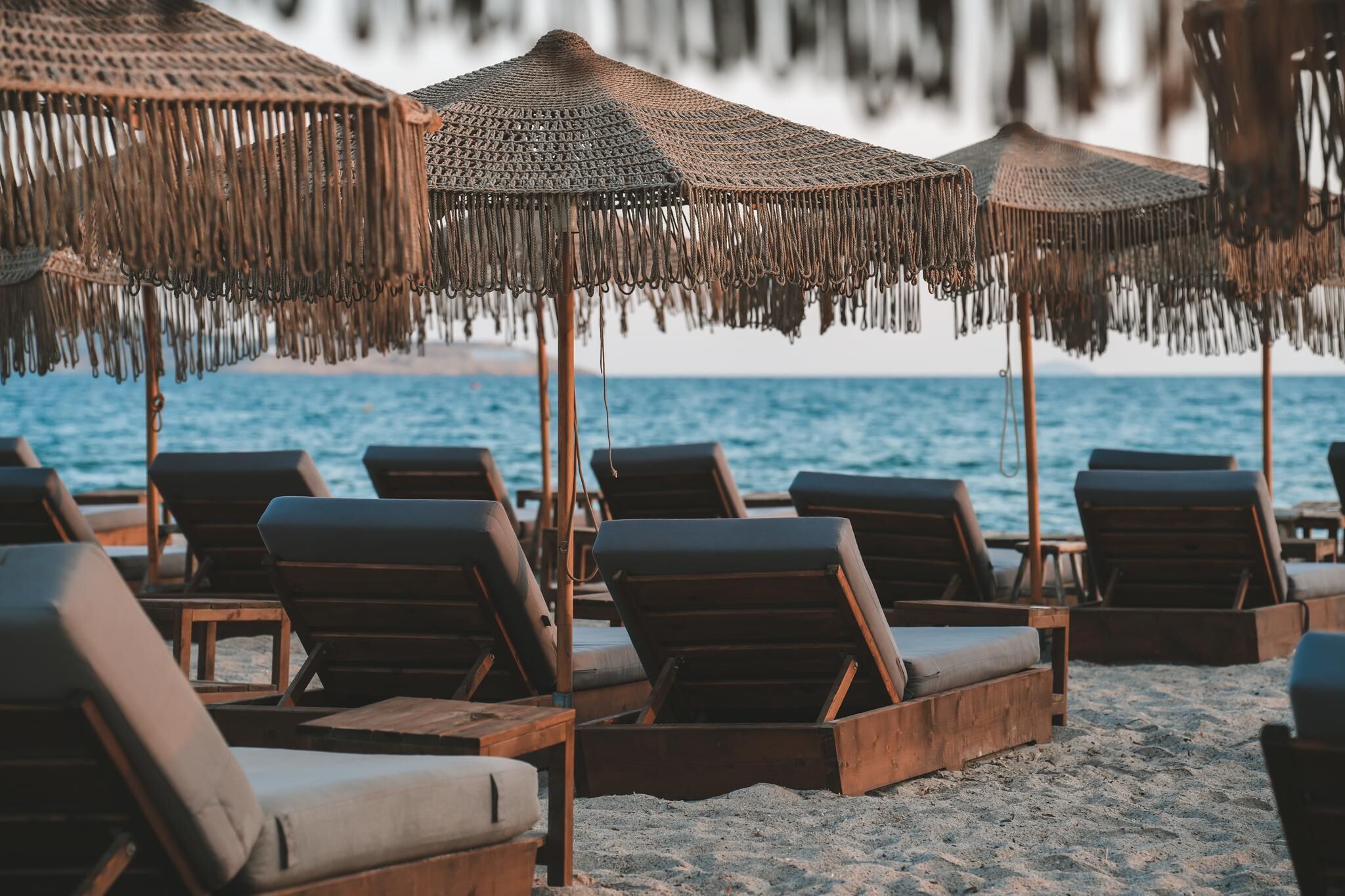 A beach with wooden lounge chairs and thatched umbrellas.