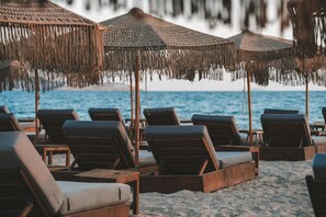 A beach with wooden lounge chairs and thatched umbrellas. - Ananea More Meni Kos ex More Meni Beach (Kos)