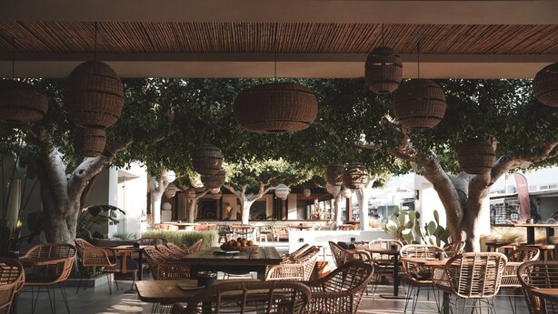 Un cafè a l'aire lliure amb moble de vimetla i cistelles penjants.