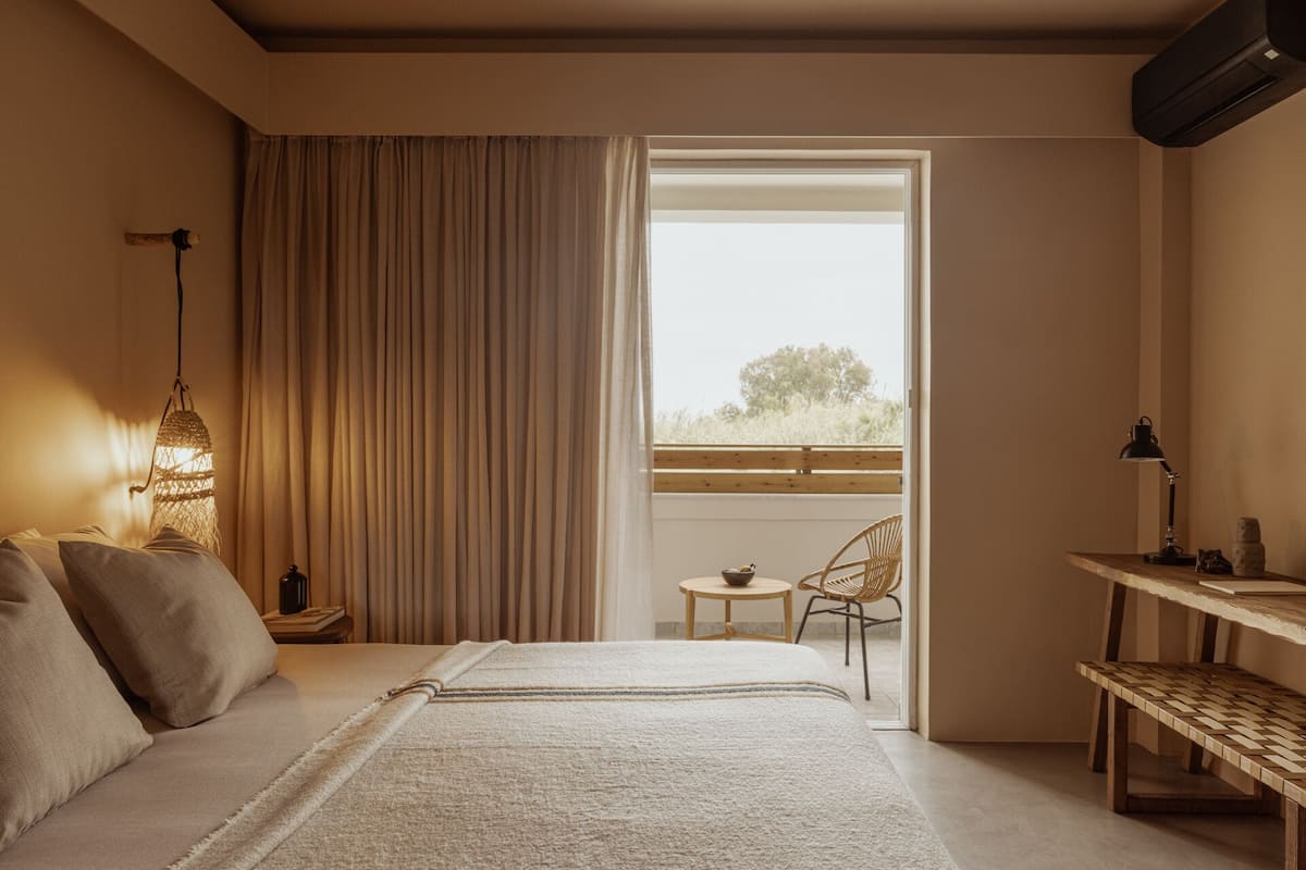 A bedroom with a bed, a desk, a chair, and a window with a view of trees.