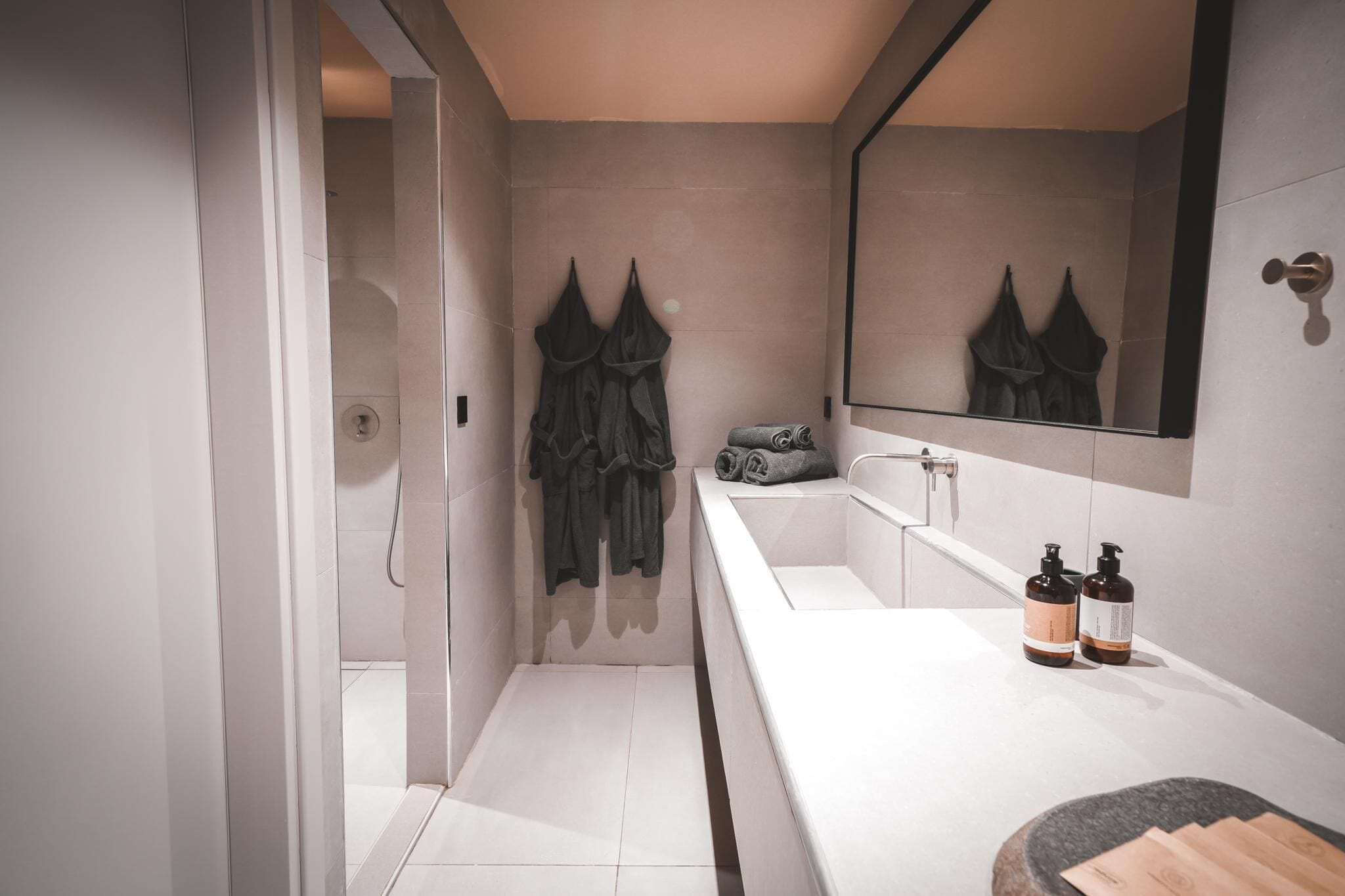 Un baño moderno con un lavamanos blanco, un espejo grande y dos botellas de champú.