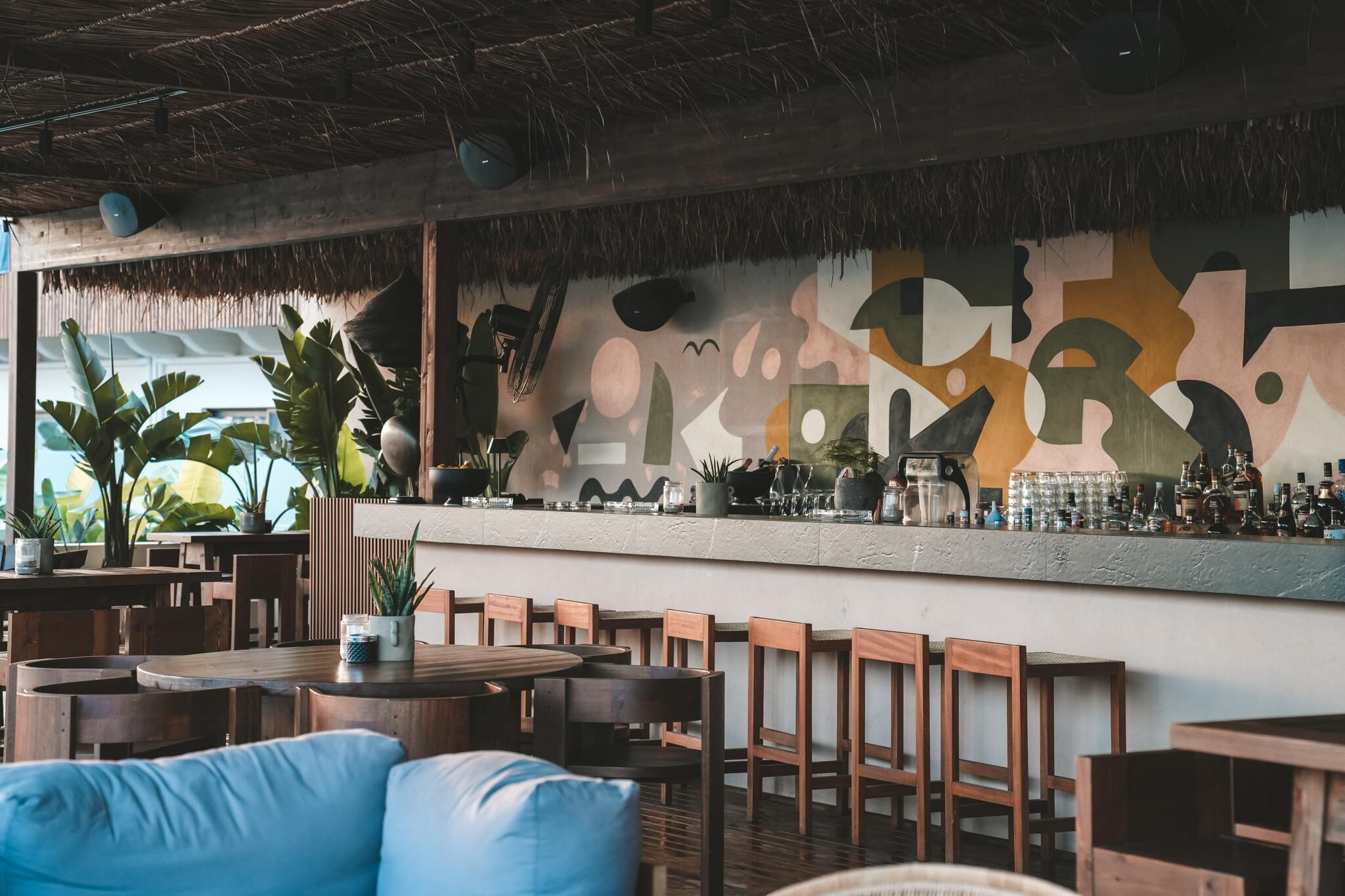 A restaurant with wooden tables and chairs, a bar area with bottles, and a mural on the wall.
