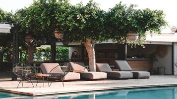 A poolside area with a sofa and chairs, a tree, and a hanging basket.