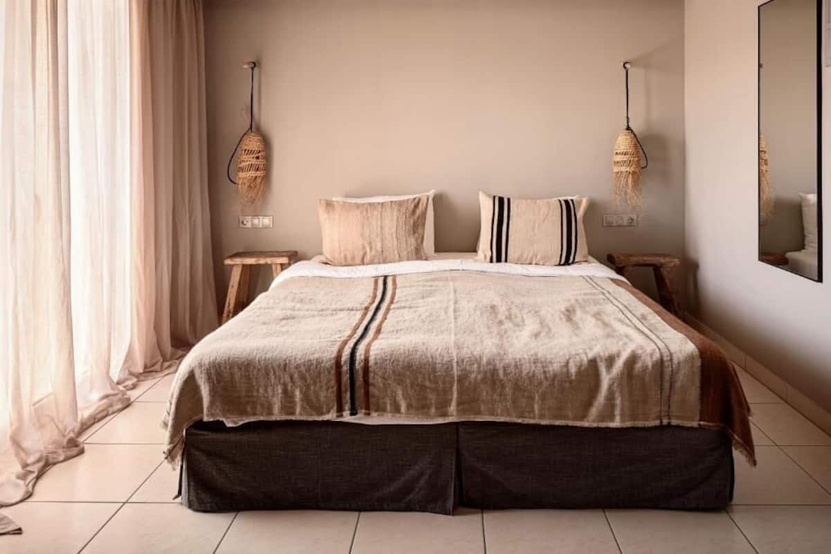 A bedroom with a bed, two bedside tables, a hanging light fixture, and a mirror on the wall.