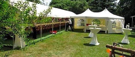 Un espacio al aire libre con césped, tiendas de campaña blancas y mesas, probablemente para un evento o reunión.