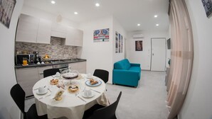 Cozinha moderna com armários brancos, mesa de jantar posta para o café da manhã e sofá verde-água na sala de estar.