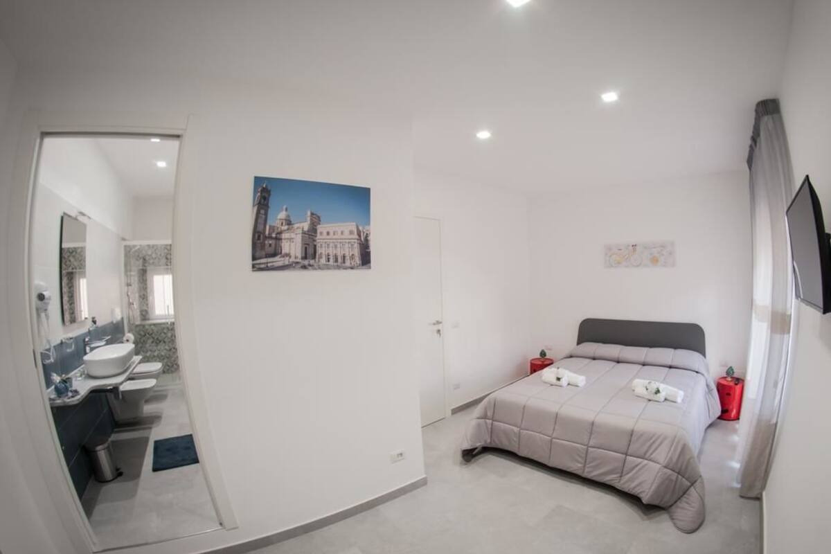 A bedroom with a bed, a bedside table, a red nightstand, and a wall-mounted TV.