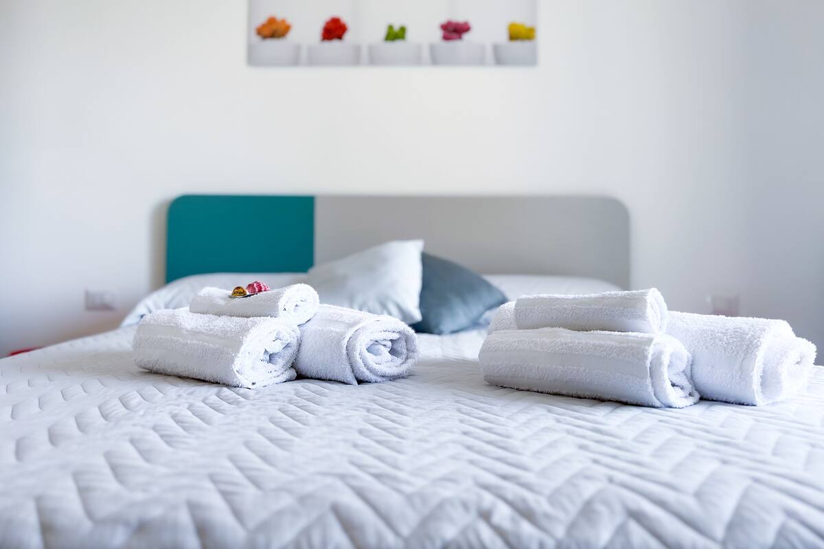 A neatly made bed with rolled white towels and a teal headboard.
