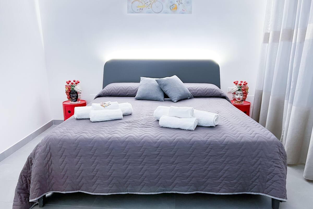A modern bedroom with a large bed, grey bedding, and two nightstands with red accents.