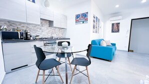 Uma cozinha moderna com armários brancos, micro-ondas e fogão. Há uma mesa de vidro com cadeiras no centro do quarto.