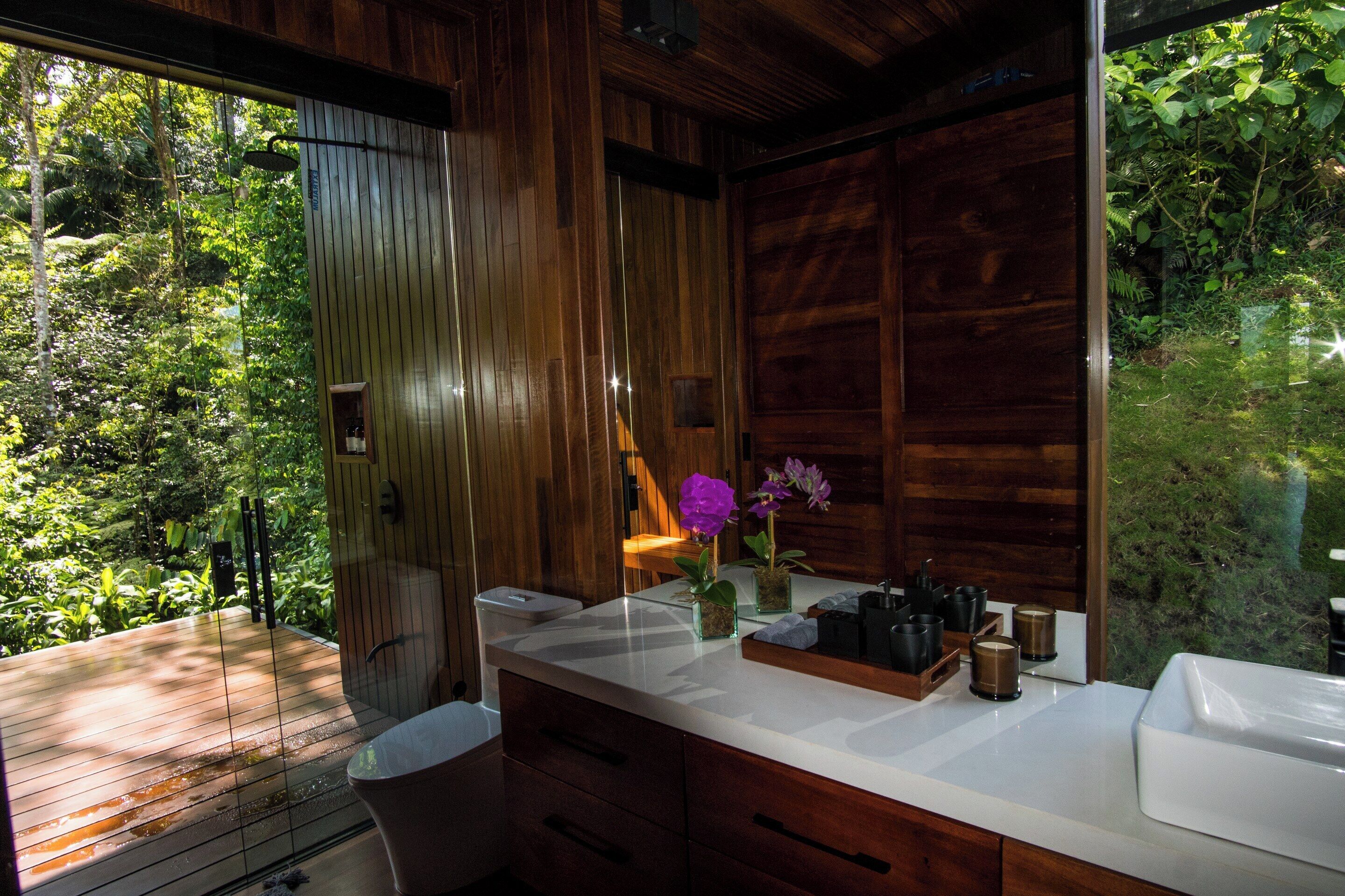 Une salle de bain au décor intérieur en bois, dotée d’un plan de toilette blanc et offrant une vue sur un jardin luxuriant.